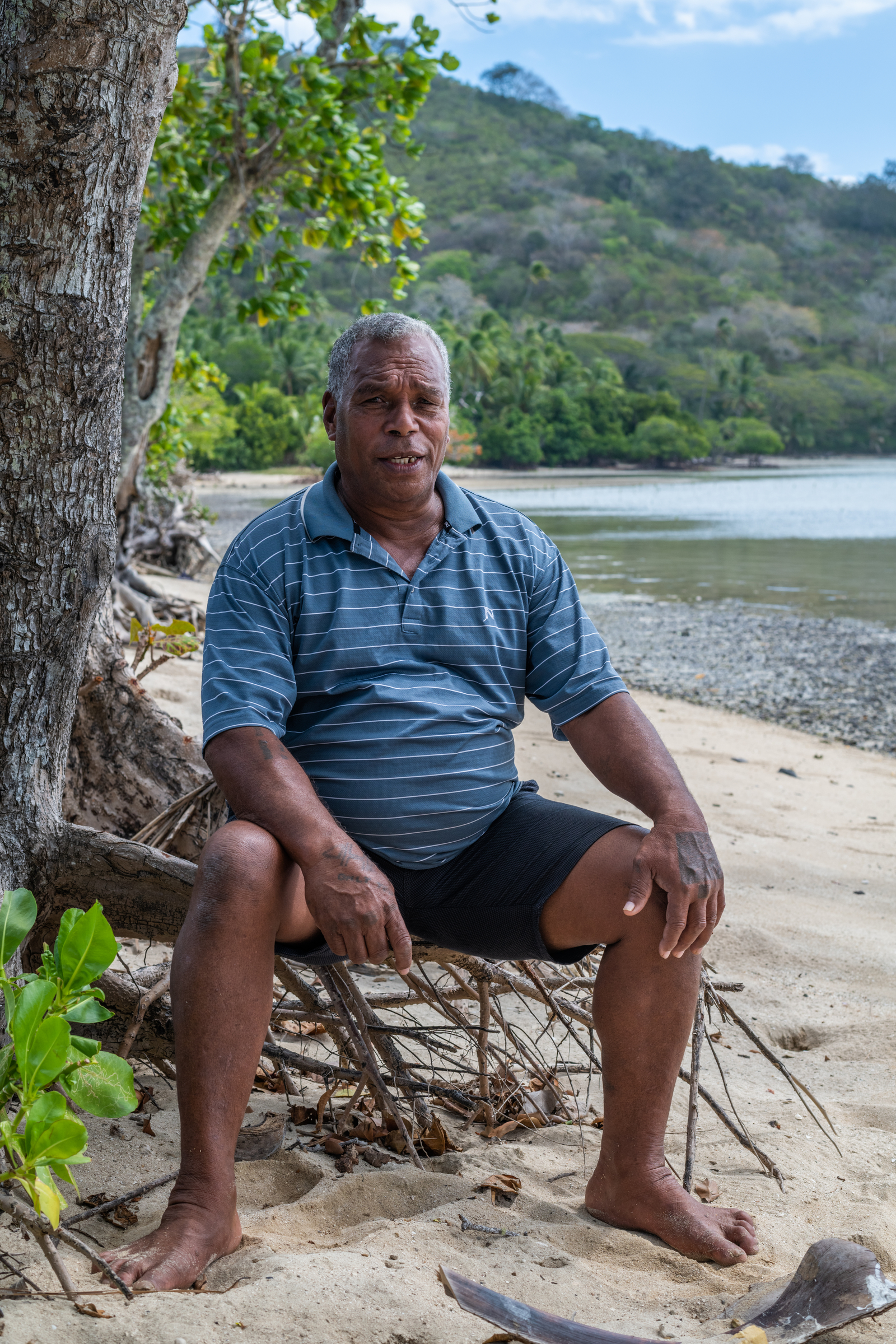 Portrait of Josateki Manatua sitting on a tree trunk in front of the Raviravi village overlooking the ocean. Raviravi, Vanua Levu, Fiji. Portrait of Josateki Manatua sitting on a tree trunk in front of the Raviravi village overlooking the ocean. Raviravi, Vanua Levu, Fiji.
