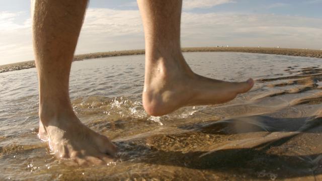 Man's bare feet walking in the water