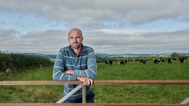 Aled, a farmer in Carmarthenshire, standing behind the gate of his field of cattle.
