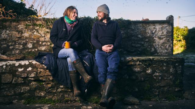 Polly and Graeme sit on a stone wall on the farm.