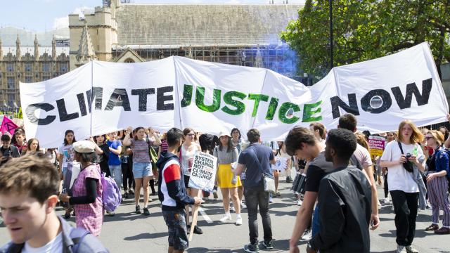 Large white banner on a march reading "climate justice now" in green and brown letters