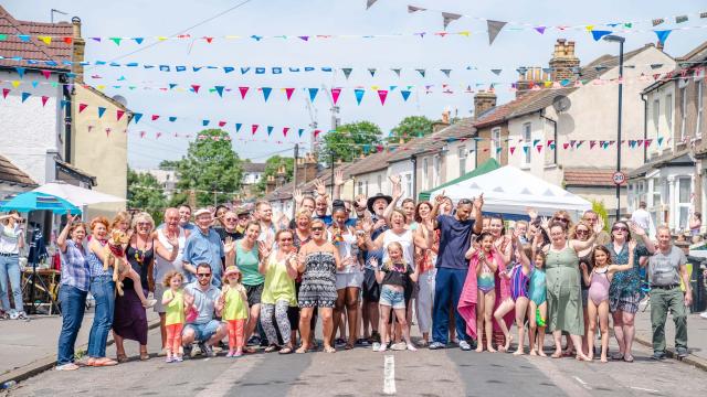 Street party on a sunny day, group photo of people on the closed road with bunting hanging over the street