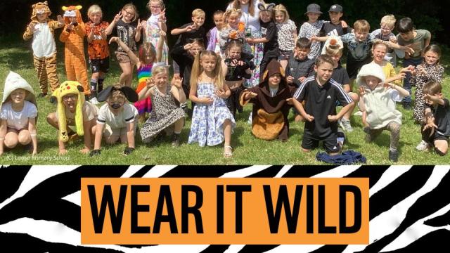 A group of school children and their teacher, dressed in animal fancy dress, in their school field. 
