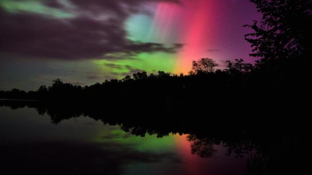 A vibrant aurora borealis display with soft pink, purple, and green lights glowing through a partially cloudy sky