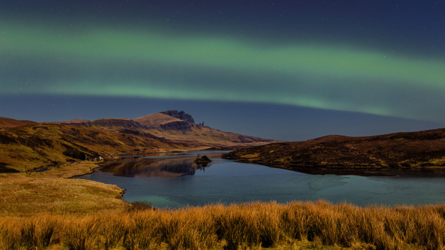 Green hues dancing across the night sky, over the Isle of Skye. The Old Man of Storr can be seen in the distance.