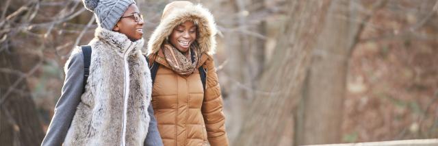 Two women walking over a bridge in nature in the winter