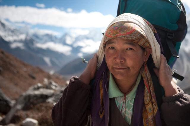 Woman carrying a heavy backpack on the road from Dengboche to Tuckla Pass, in the Everest region of the Himalayas in Nepal.