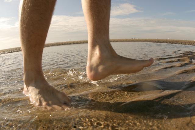 Man's bare feet walking in the water.