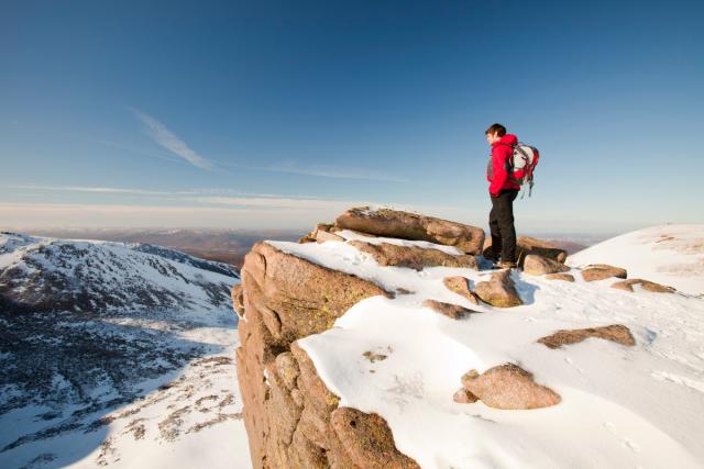 A mountaineer on a rocky granite outcrop above Coire an Lochain in the Cairngorm Mountains, Scotland, UK.