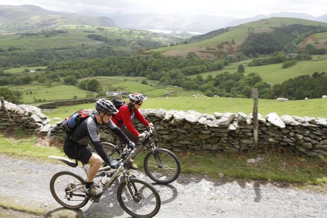 Two people cycling on a small road. A scenic countryside landscape behind them,