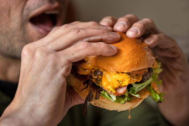 Man about to eat a beef burger with bacon, cheese and lettuce, London, UK. 