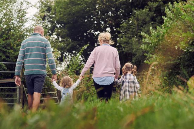 The family at Rest Farm, both parents and two children, walk through the field long the hedgerow.