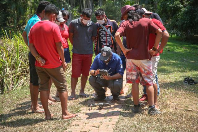 A group of nine Indigenous People watching a demonstration of how to use a drone