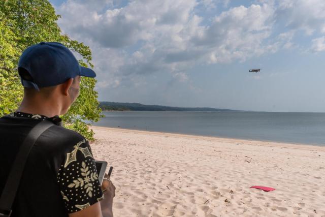 An Indigenous man flying a drone across the beach
