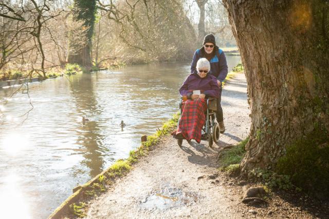 Elderly couple, lady in wheelchair, along riverside in winter