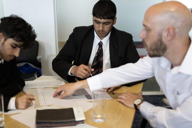 Two school children and a teacher sat at a table writing