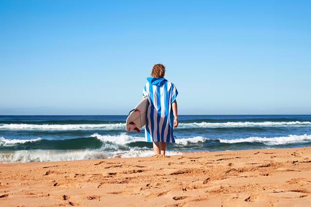 Poncho Blue on guy walking towards ocean with a surf board