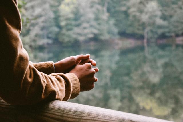 Arms resting on wooden fence over overlooking lake