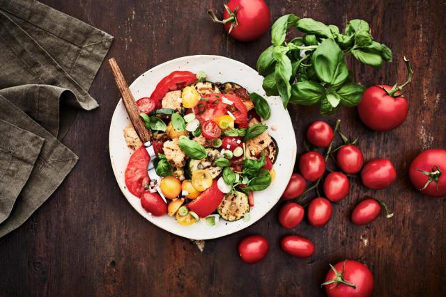 An plate of panzanella salad with basil and tomatoes on the side
