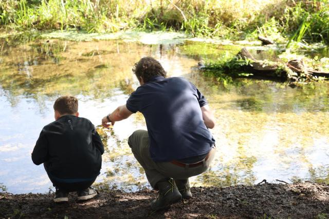 Man and boy crouched next to a river