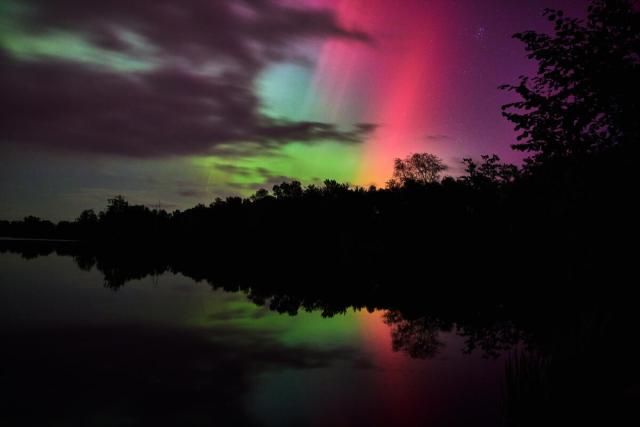 A vibrant aurora borealis display with soft pink, purple, and green lights glowing through a partially cloudy sky
