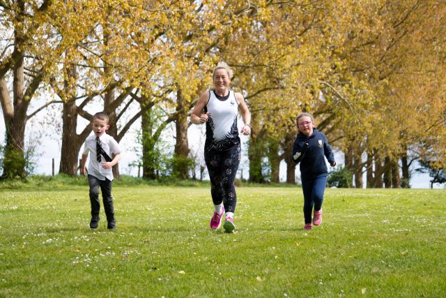 A group of school children and their teacher, running, in their school field. 