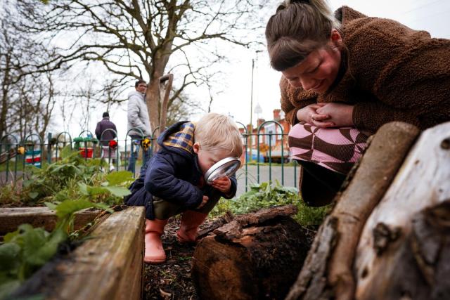 Little boy looking through magnified glass in Belgrave Community inner-city garden in Leicester