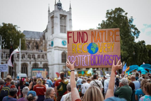 A crowd protesting and a placard saying 'fund nature recovery protect biodiversity'