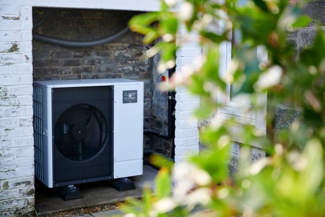 A heat pump on the side of an Edinburgh home. Green foliage in the forefront.