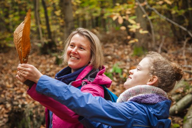 A mother and daughter looking at a leaf in a forest in autumn. 