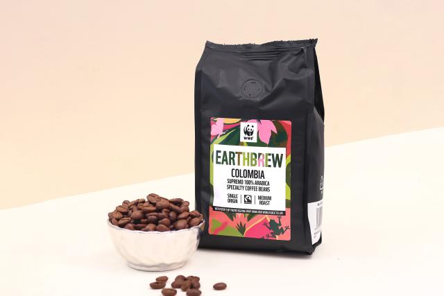 A bag of WWF Earthbrew coffee behind a bowl of coffee beans