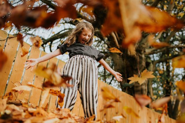 Autumn leaves scatter, falling towards the camera, surrounding a young girl © Catherine Falls Commercial / Getty Images