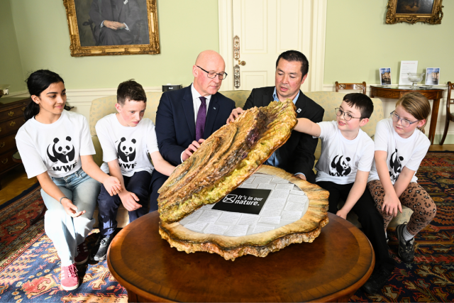 A group of young nature supporters and Lang Banks, Director of WWF Scotland, handover messages for nature and climate to John Swinney, First Minister, at Bute House. These messages are presented in a giant papier-mache oyster which the First Minister and young people are opening in the photograph.