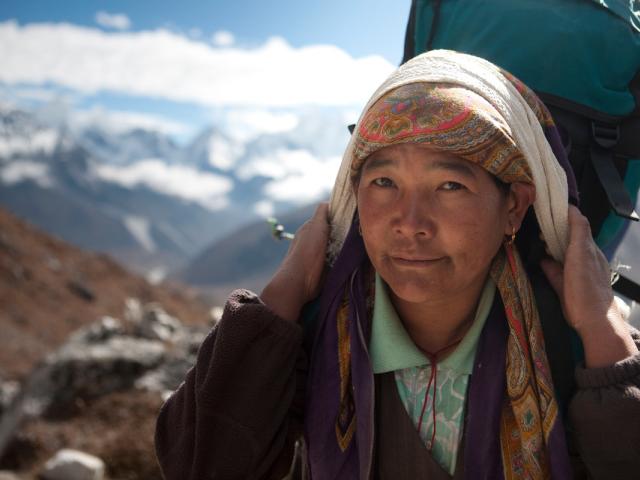 Woman carrying a heavy backpack on the road from Dengboche to Tuckla Pass, in the Everest region of the Himalayas in Nepal.