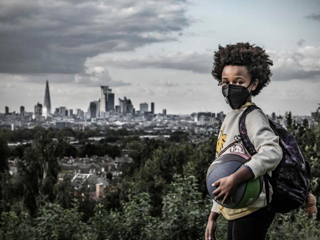 Afrika, 8, holds a ball and wears a mask to protect against air pollution. Dawson Heights, south east London.