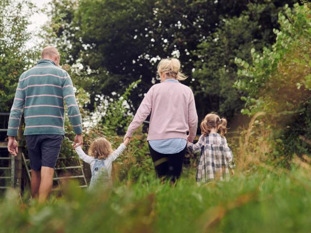 The family at Rest Farm, both parents and two children, walk through the field long the hedgerow.