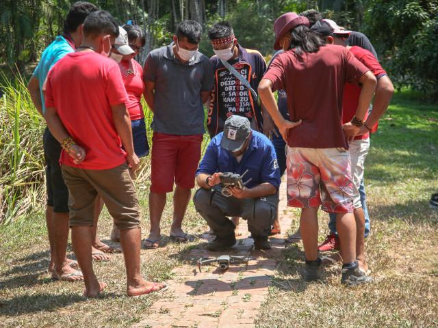 A group of nine Indigenous People watching a demonstration of how to use a drone
