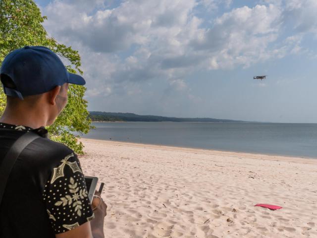 An Indigenous man flying a drone across the beach