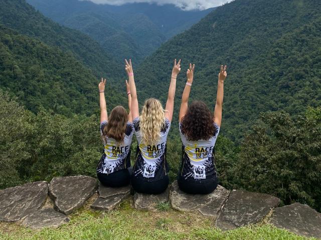 Three people, looking over the rainforest in Colombia, with their arms in the air. 