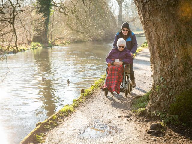 Elderly couple, lady in wheelchair, along riverside in winter
