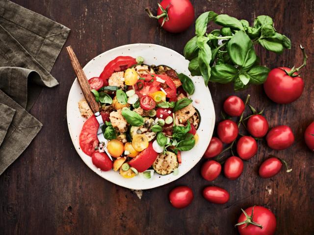 An plate of panzanella salad with basil and tomatoes on the side