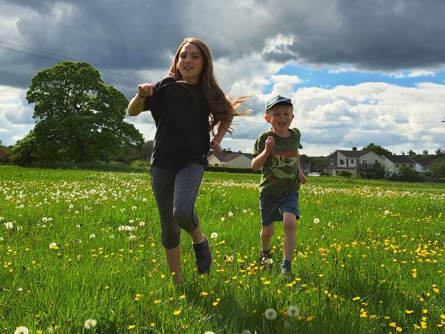 Two kids running in field opposite some houses