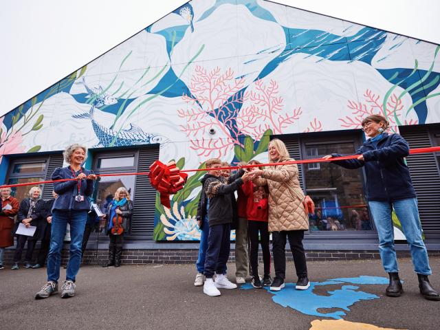 People cutting a red ribbon in front of a mural