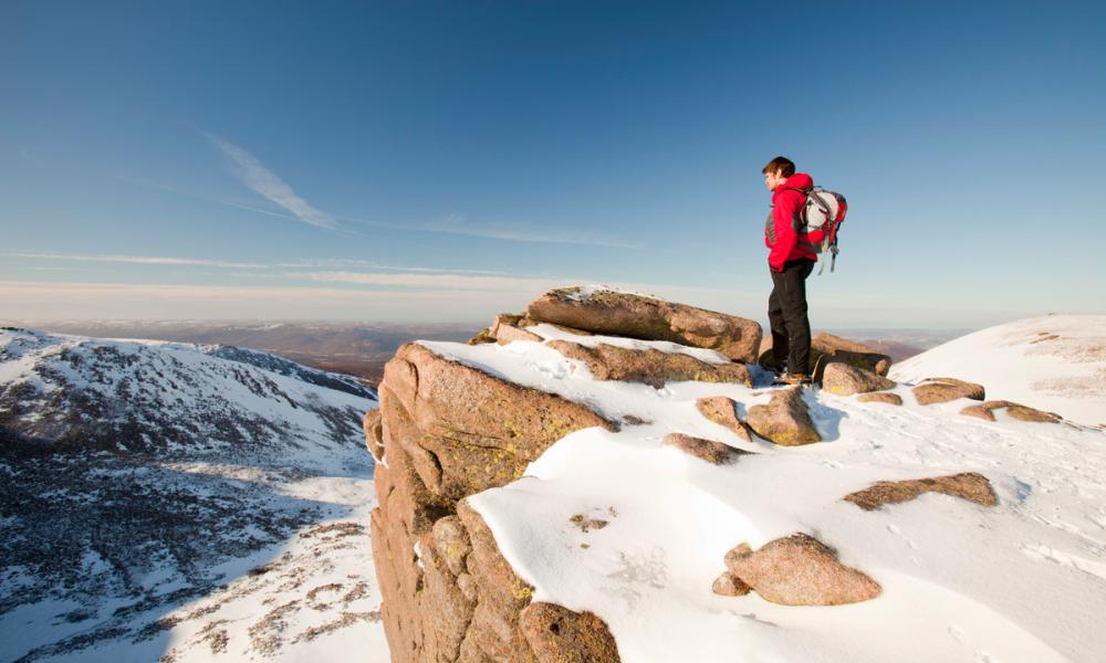 A mountaineer on a rocky granite outcrop above Coire an Lochain in the Cairngorm Mountains, Scotland, UK.