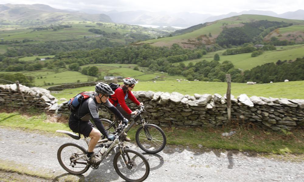 Two people cycling on a small road. A scenic countryside landscape behind them,