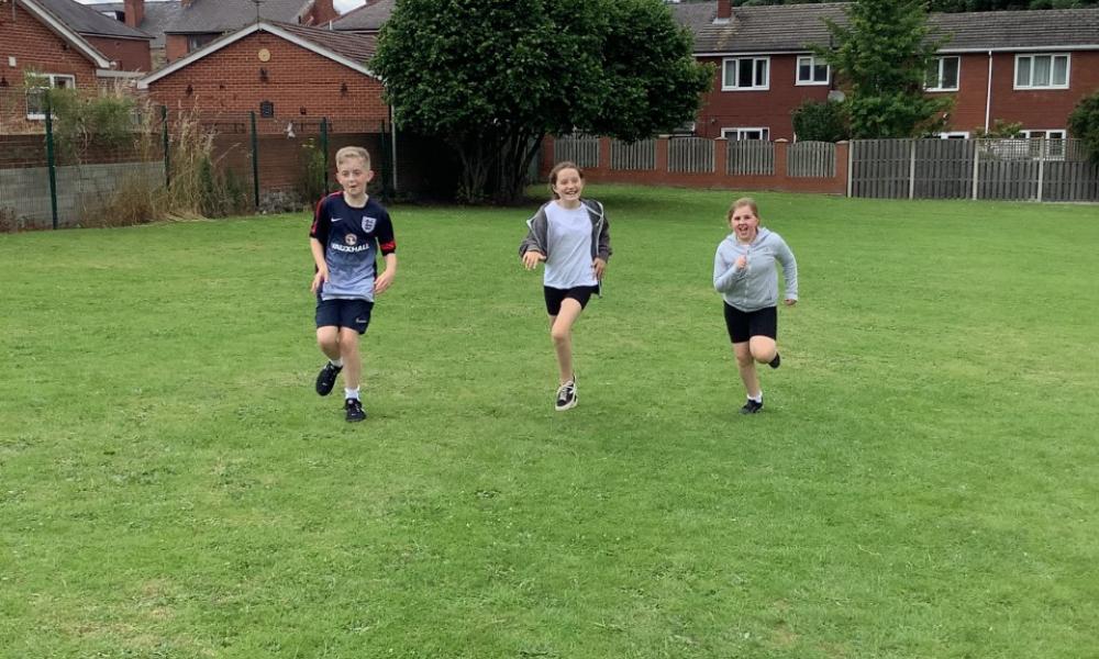 Three students, running towards the camera, in their school field