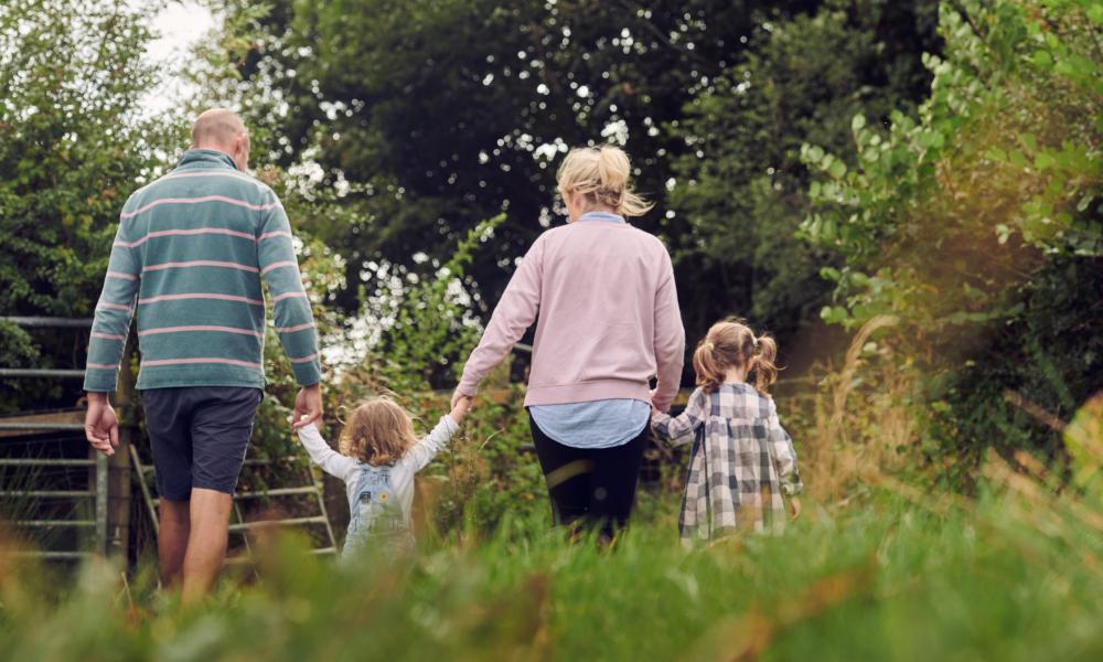 The family at Rest Farm, both parents and two children, walk through the field long the hedgerow.