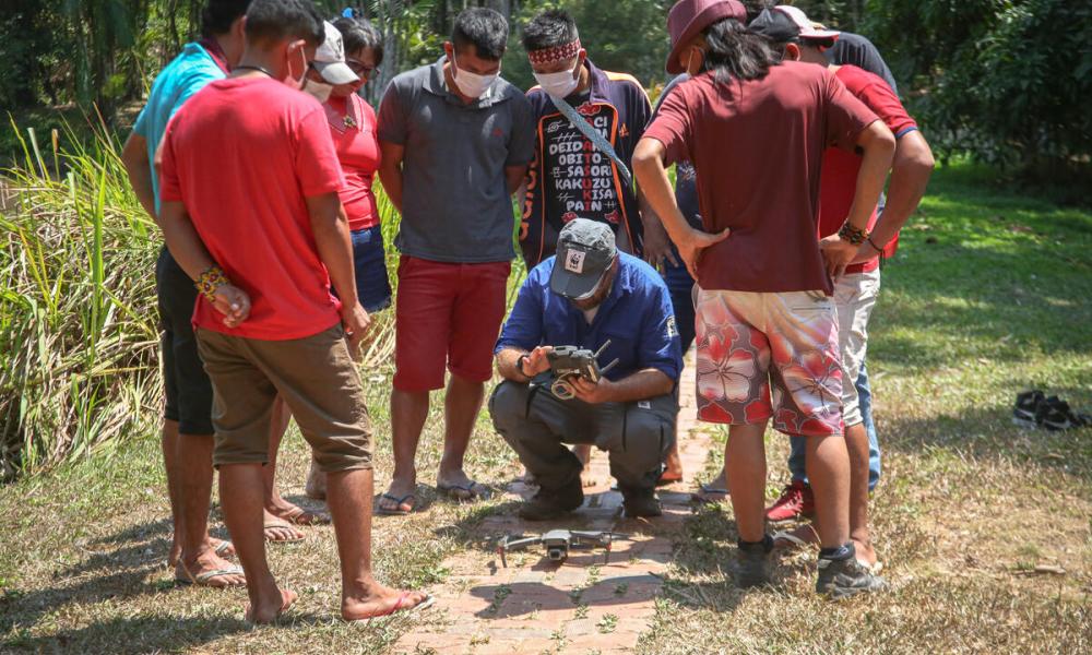 A group of nine Indigenous People watching a demonstration of how to use a drone