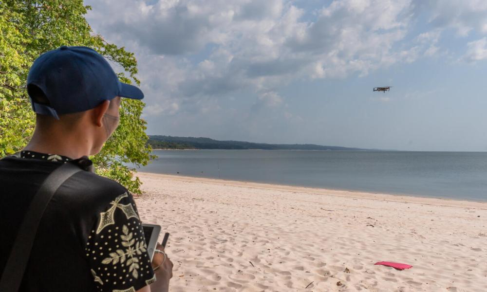 An Indigenous man flying a drone across the beach