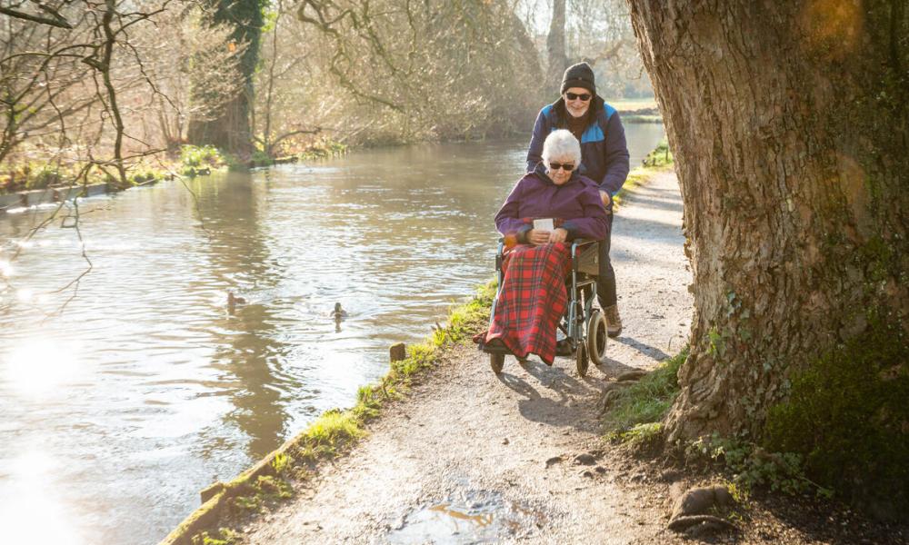 Elderly couple, lady in wheelchair, along riverside in winter